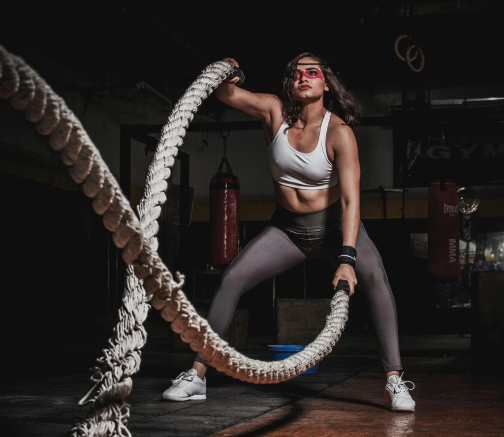 Female athlete demonstrating strength with battle ropes in a gym.