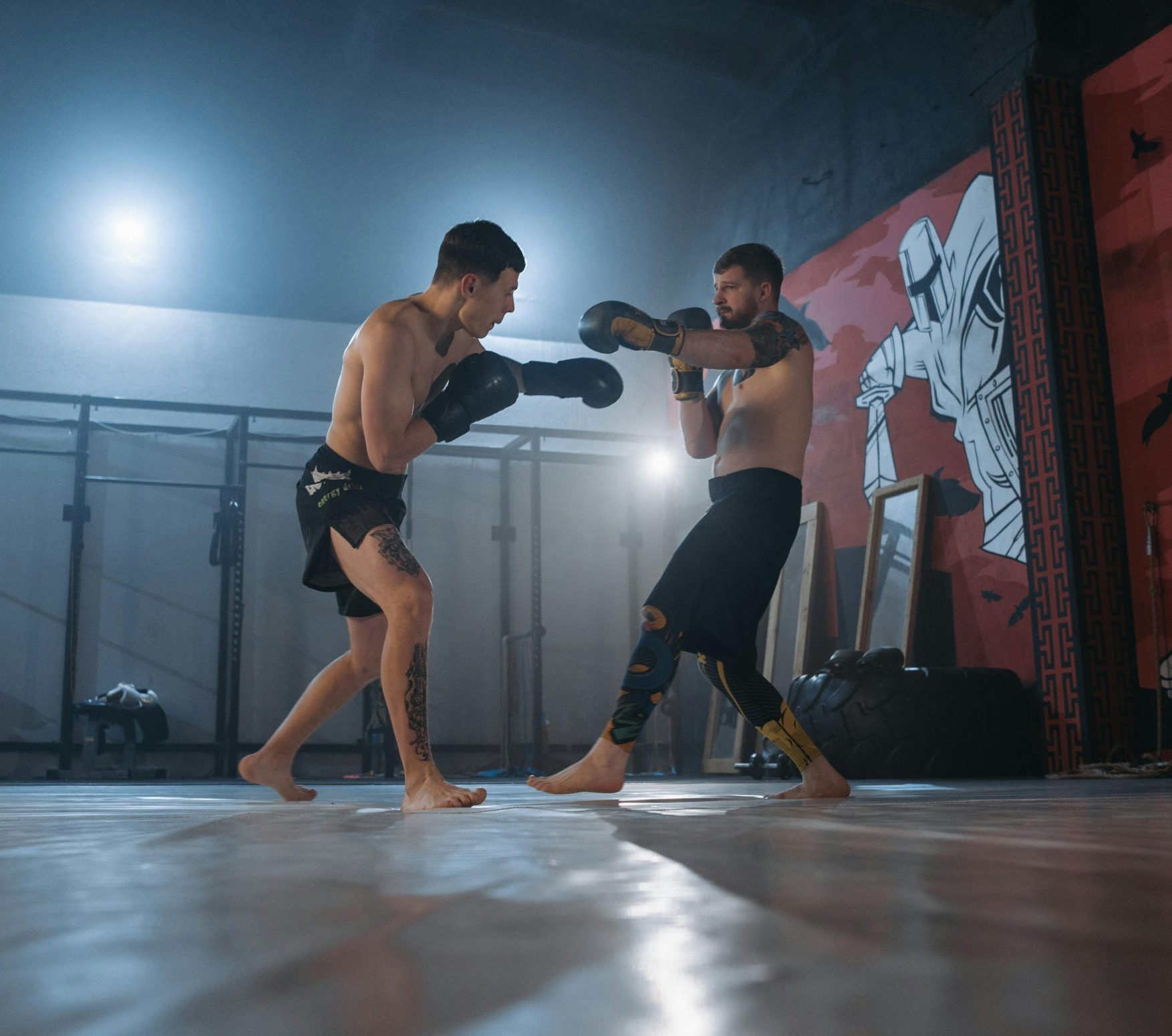 Two fighters engage in MMA sparring in a well-equipped gym setting.