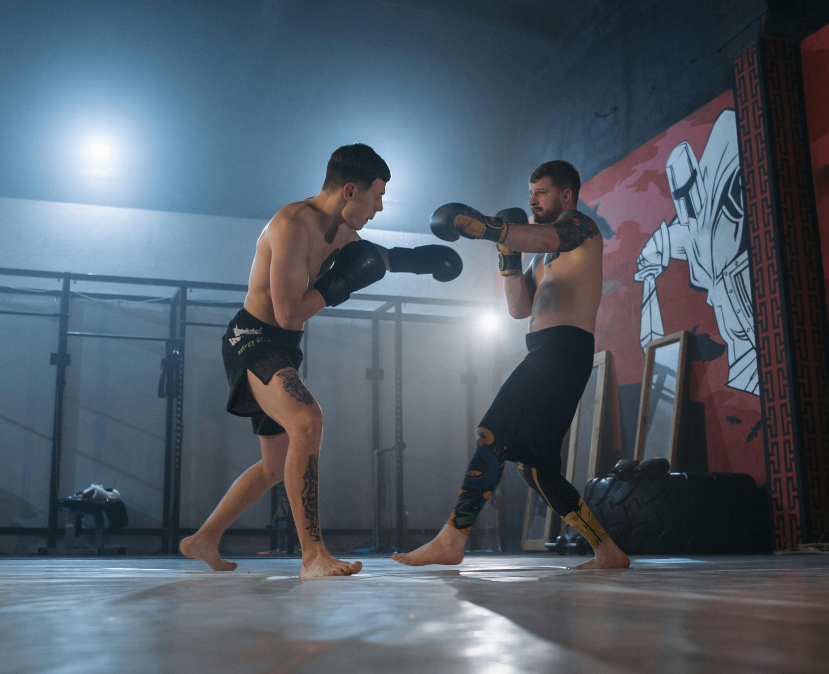 Two fighters engage in MMA sparring in a well-equipped gym setting.