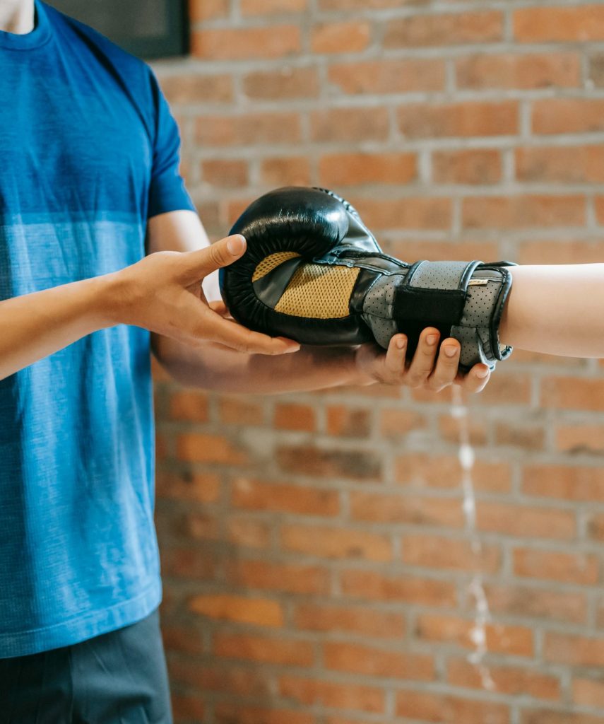 Trainer assisting client with boxing gloves in a gym setting.